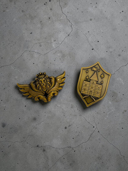 Two gold-toned metal page clips: lion crest winged badge and shield crest