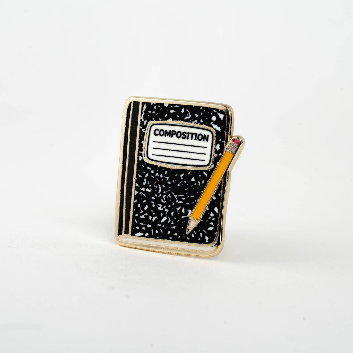 Enamel composition notebook pin with black notebook, 'COMPOSITION' label, and orange pencil