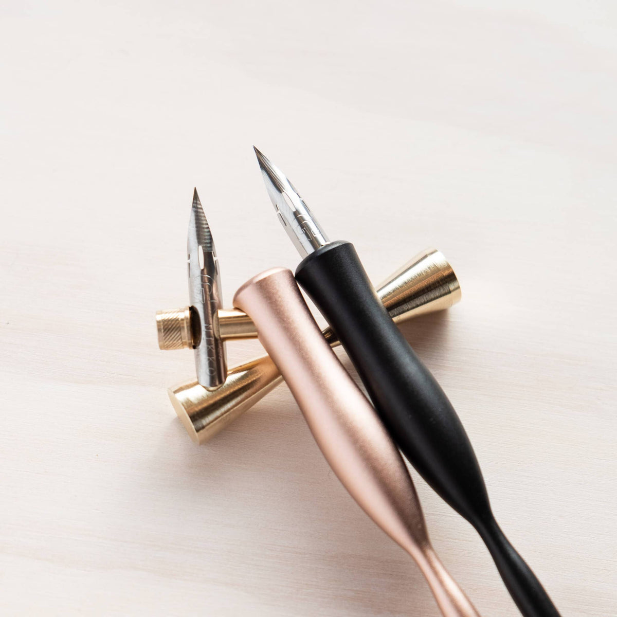 Brass pen rest holding two pens with black and rose-gold bodies and pointed tips