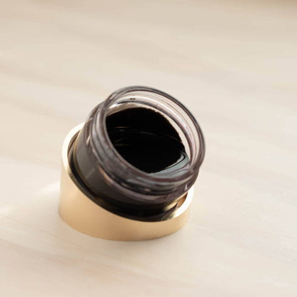 Tilt ink pot holder close-up with gold rim and clear glass cup filled with dark ink