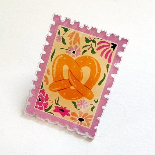 Square acrylic magnet, angled view; pink scalloped border with orange pretzel floral artwork