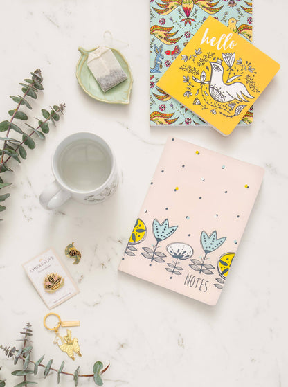 Floral bird enamel pin shown beside its backing card and a matching bird keychain.