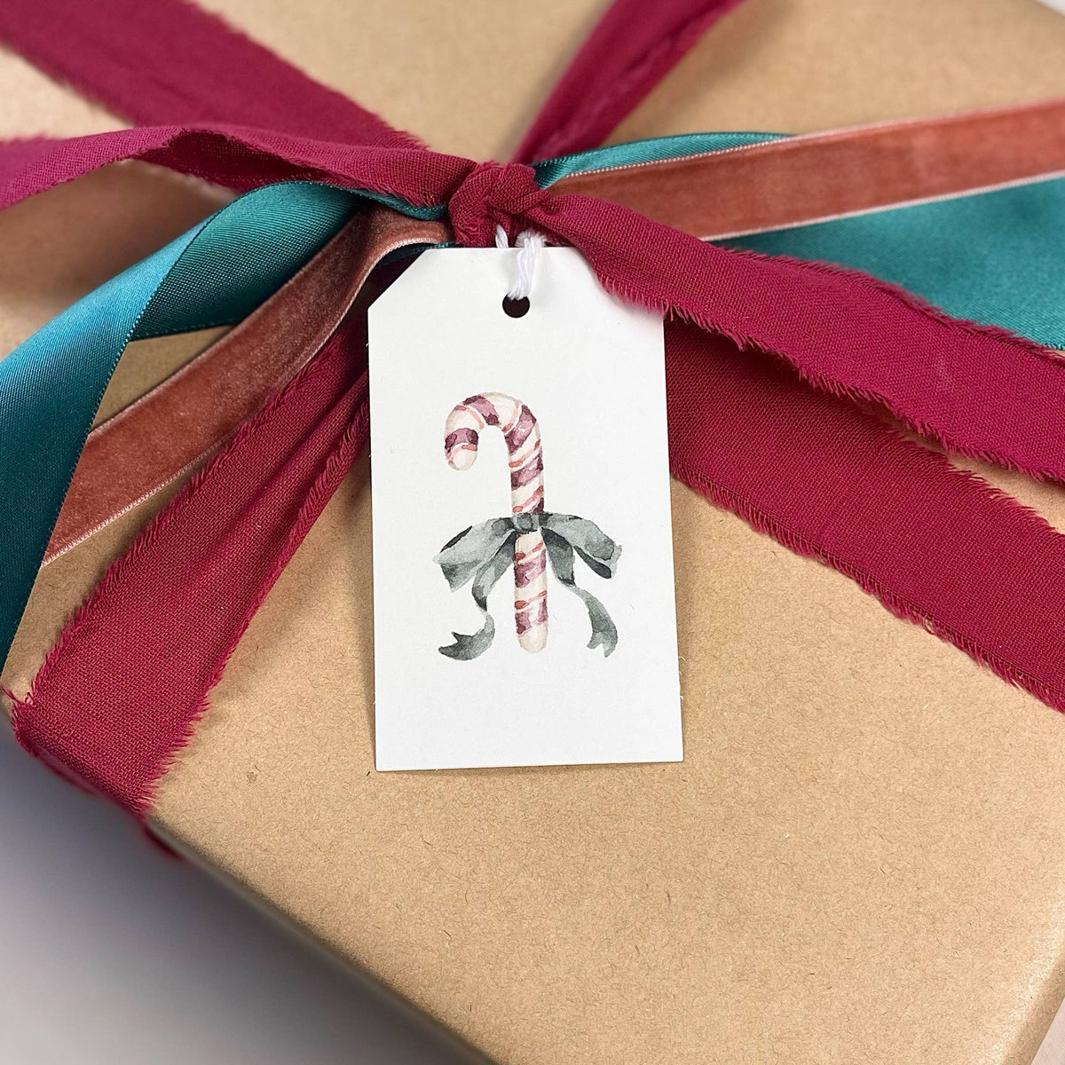 Candy cane gift tag with holly illustration tied to wrapped present with ribbon
