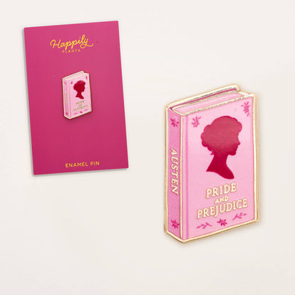 Pink book-shaped enamel pin with red silhouette, shown with 'Happily Plants' card.