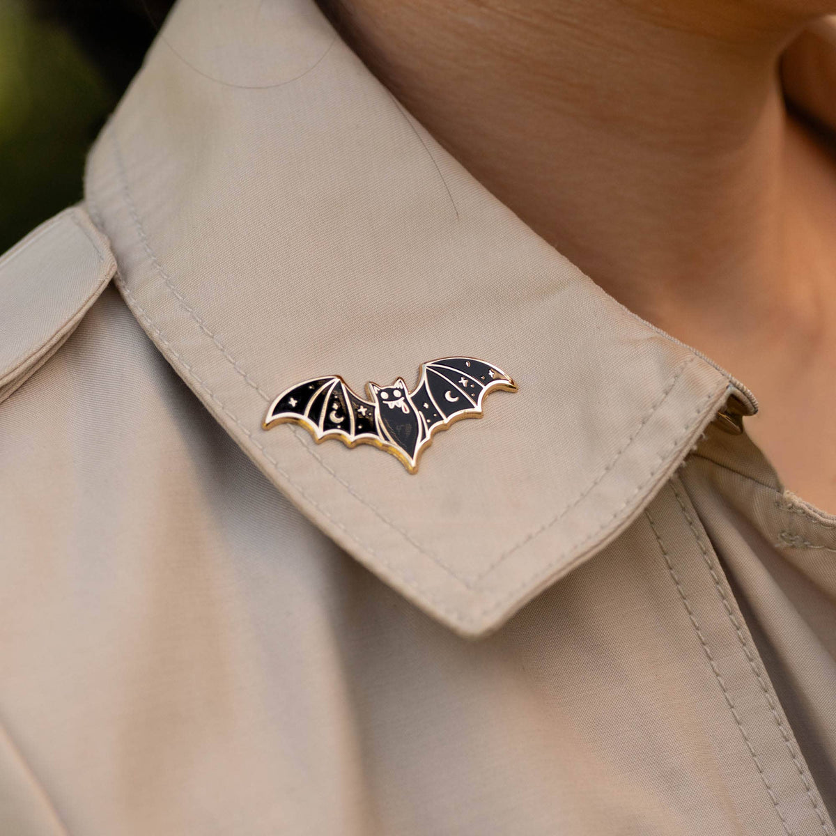 Vampire bat enamel lapel pin on light shirt collar, black wings with gold outline