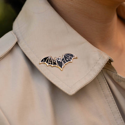 Vampire bat enamel lapel pin on light shirt collar, black wings with gold outline