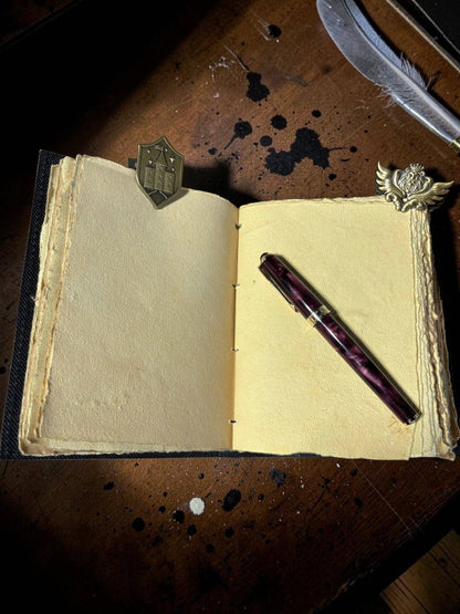 Set of 2 gold-toned metal page clips on an open notebook with a pen