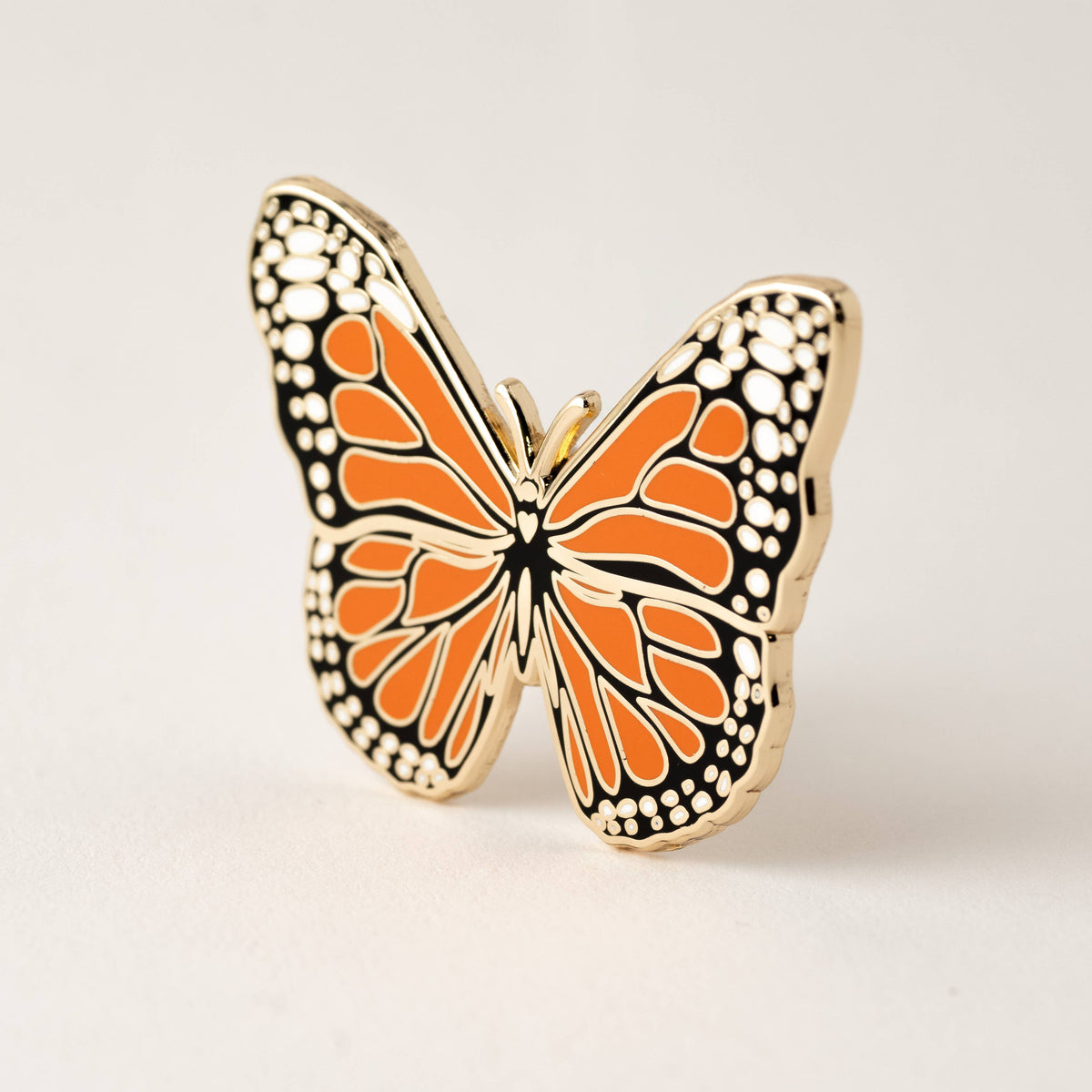 Monarch butterfly enamel pin with orange wings and gold-tone border.