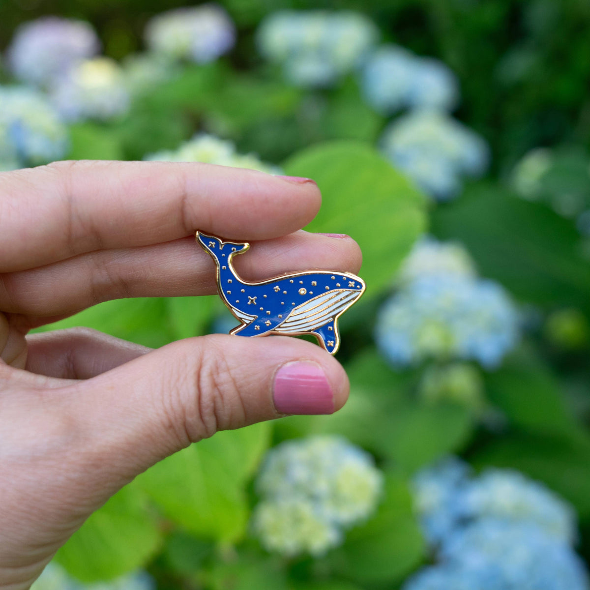 Blue whale enamel pin held in hand, navy body with gold trim