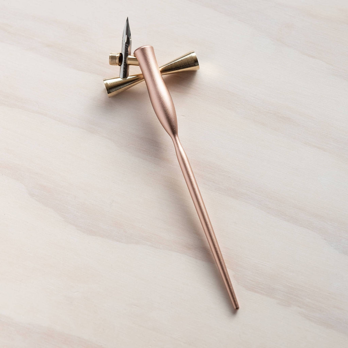 Brass pen rest holding a rose-gold pen, supported by twin conical brass parts