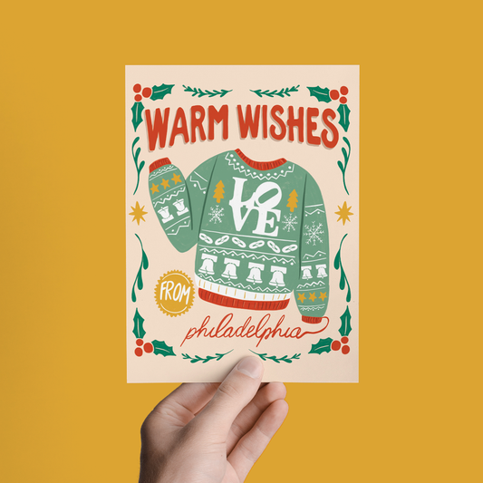 Hand-held holiday greeting card with green sweater “Warm Wishes” and “from philadelphia”