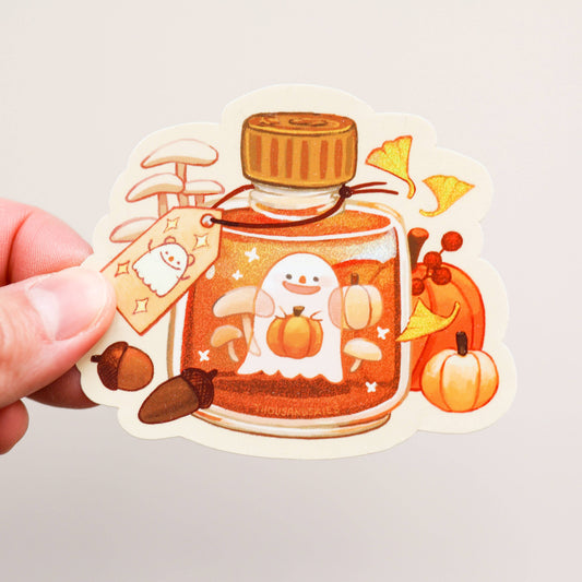 Die-cut vinyl sticker held by fingers; orange potion bottle with pumpkins, stars, and ghost