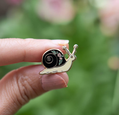 Snail enamel lapel pin in hand, black swirl shell with flower accent, gold-tone finish