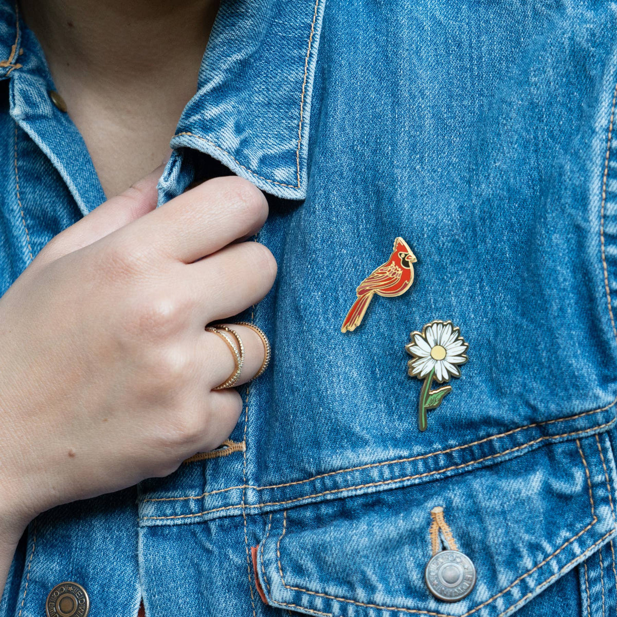 Red cardinal enamel lapel pin on blue denim jacket pocket