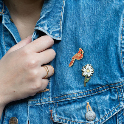 Red cardinal enamel lapel pin on blue denim jacket pocket