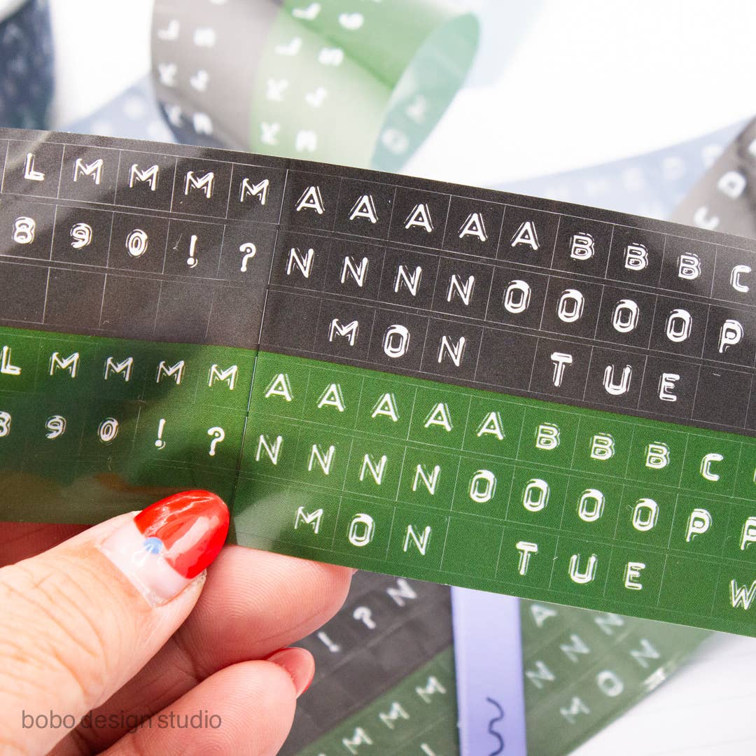 Embossed letters PET tape strip, black backing with green cut-out letter shapes