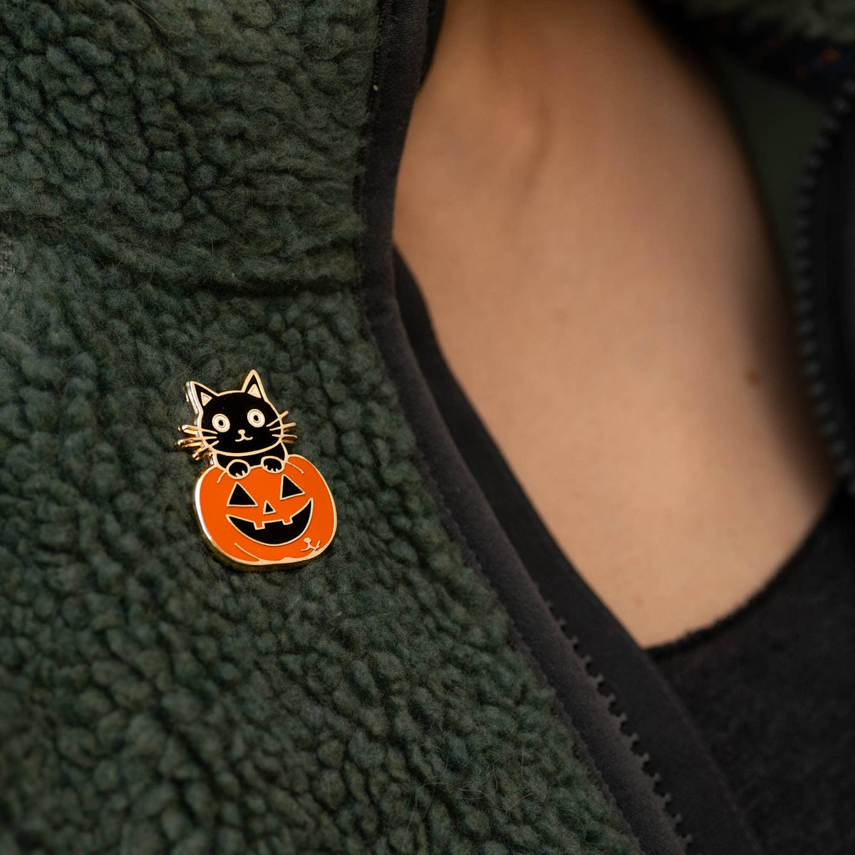 Enamel Halloween cat pumpkin pin on dark green fleece jacket