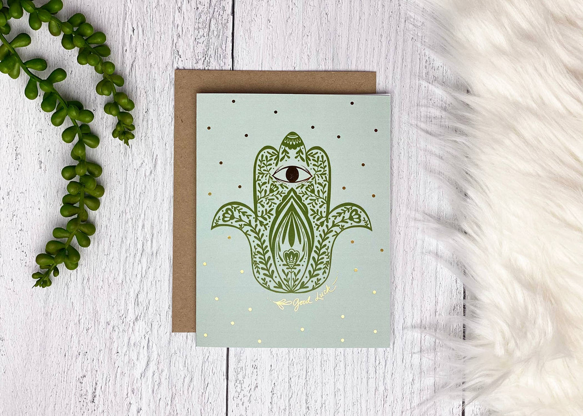 Hamsa greeting card with green hand artwork, gold foil accents, and kraft envelope
