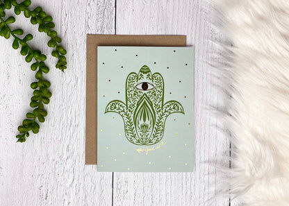 Hamsa greeting card with green hand artwork, gold foil accents, and kraft envelope