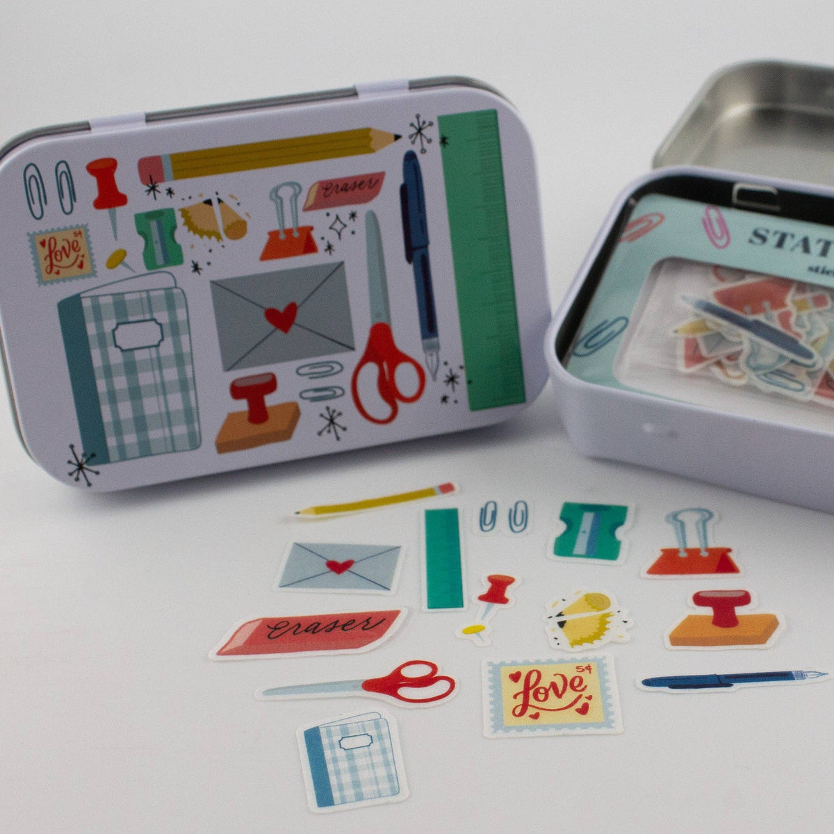 Stationery trinket tin with illustrated lid, open tray, and scattered sticker flakes