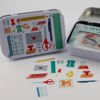 Stationery trinket tin with illustrated lid, open tray, and scattered sticker flakes
