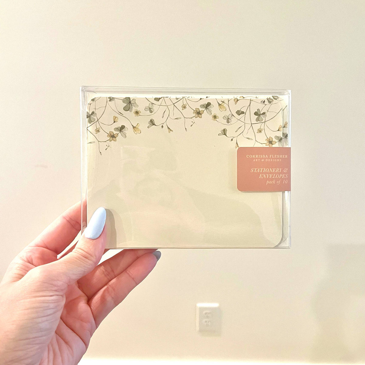 Cream botanical floral stationery envelope in a clear sleeve, held by hand