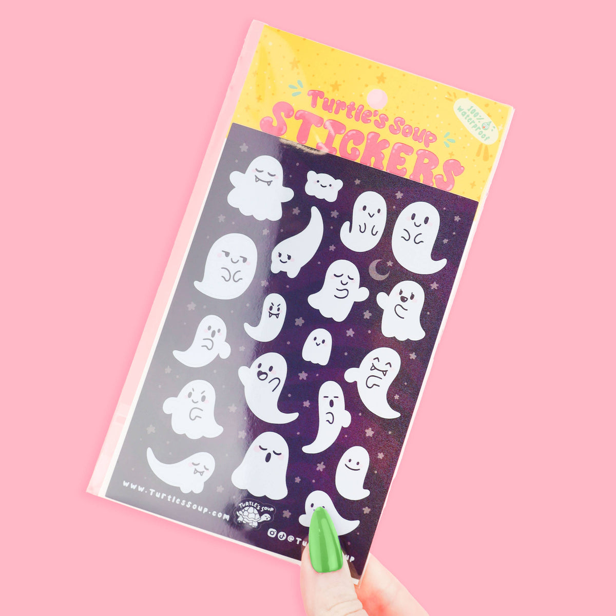 Cute ghost sticker sheet held in hand, featuring many smiling white ghosts