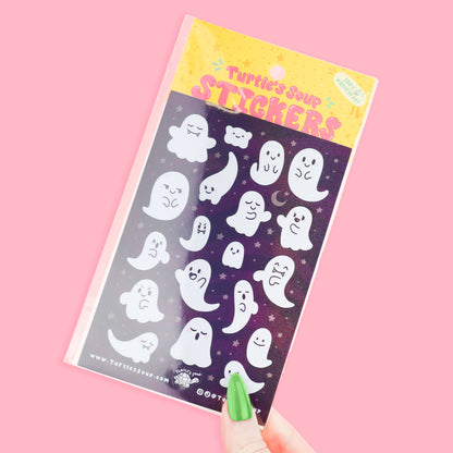 Cute ghost sticker sheet held in hand, featuring many smiling white ghosts