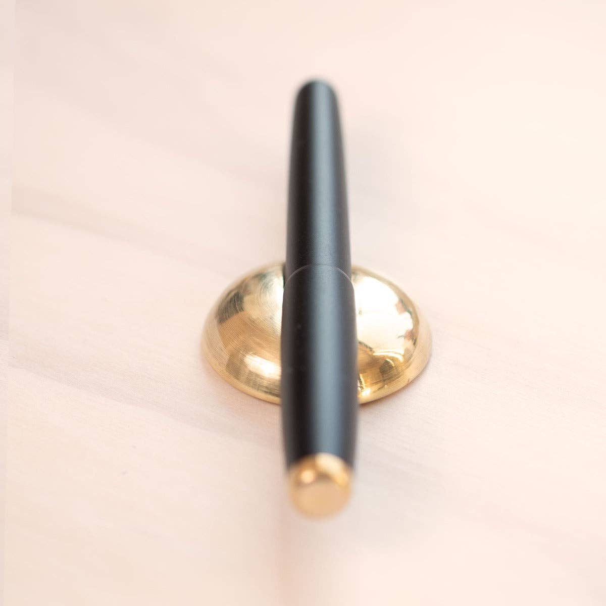 Solid brass pen rest holding a black pen upright