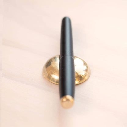 Solid brass pen rest holding a black pen upright
