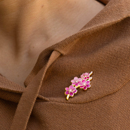 Pink cherry blossom enamel pin on a brown knit sweater